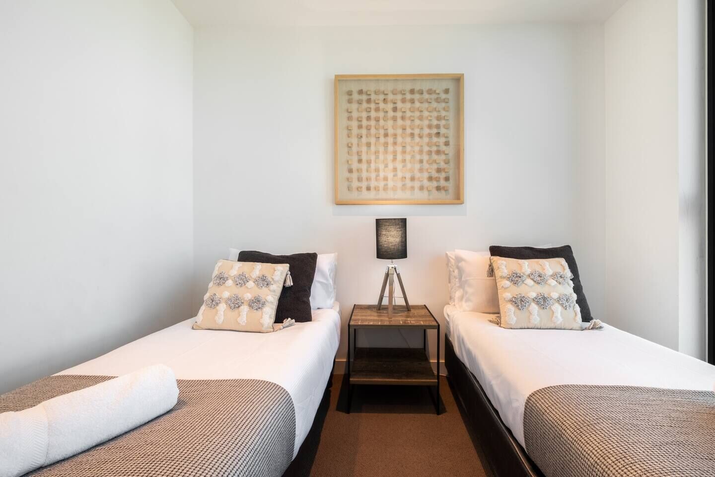 Una habitación con dos camas, una mesita con una lámpara y una obra de arte enmarcada en la pared.