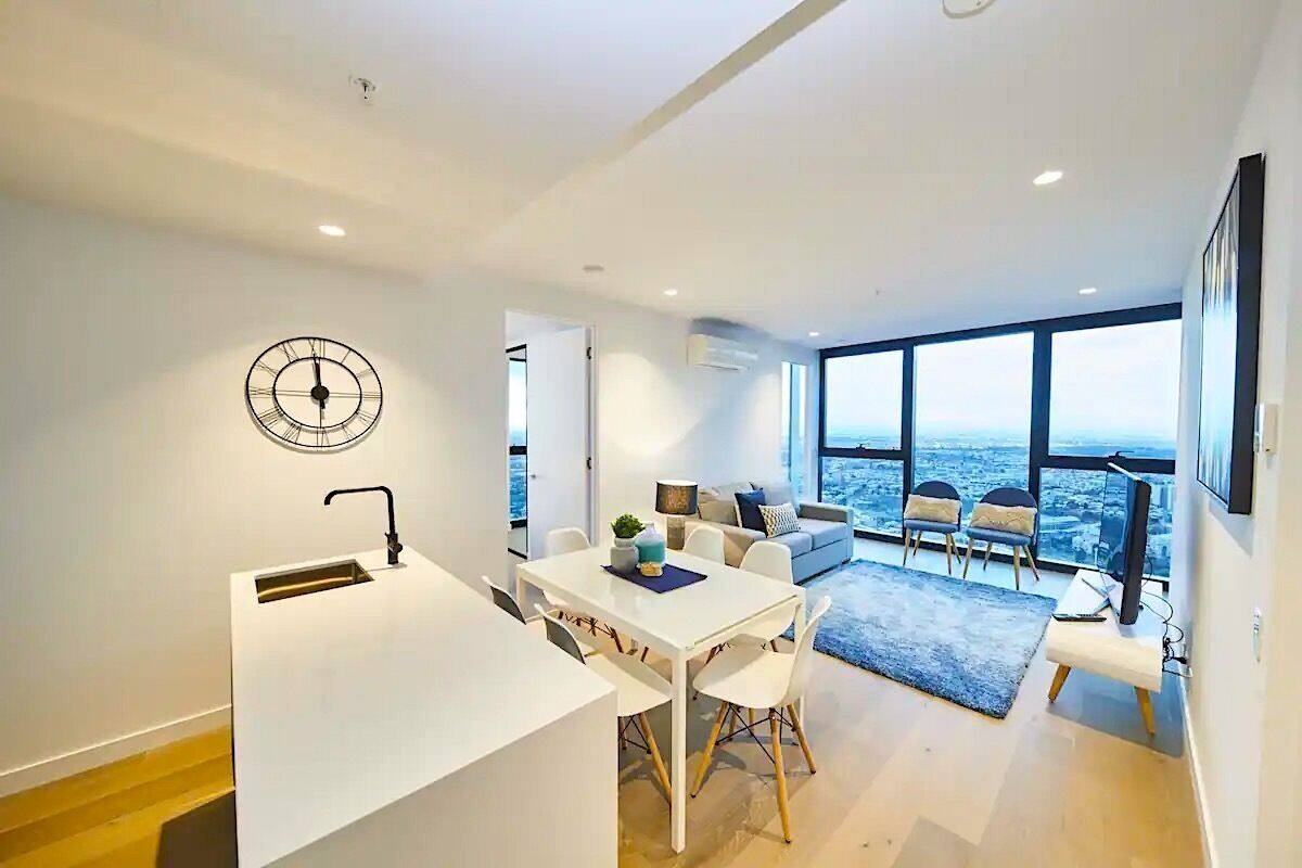 A modern kitchen with a white countertop and a sink, a dining area with a white table and chairs, and a living area with a sofa and chairs.
