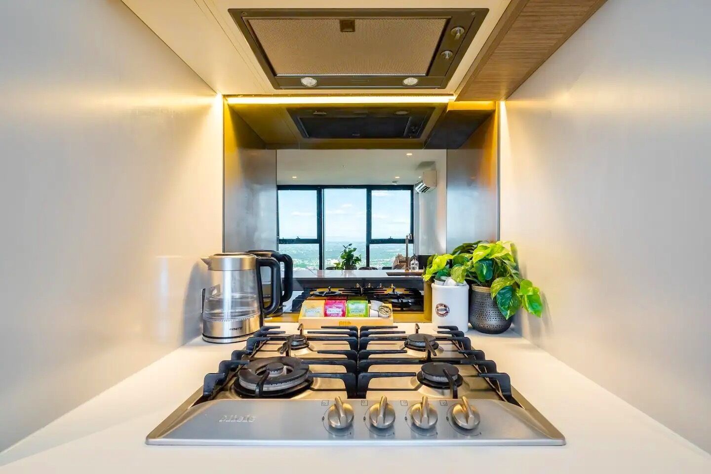 A modern kitchen with a gas stove, a coffee maker, and a view of the city.