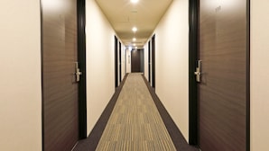 A hotel hallway with carpeted floors, wooden doors, and a ceiling light fixture. - Hotel Livemax Shinjuku East (Tokyo)