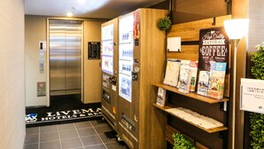 A hotel reception area with a vending machine, a coffee station, and a wooden display shelf with brochures. - Hotel Livemax Shinjuku East (Tokyo)
