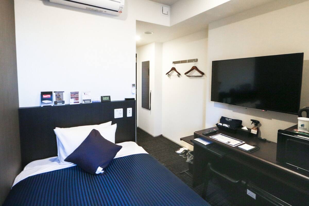 A hotel room with a bed, a desk, a TV, and an air conditioning unit.
