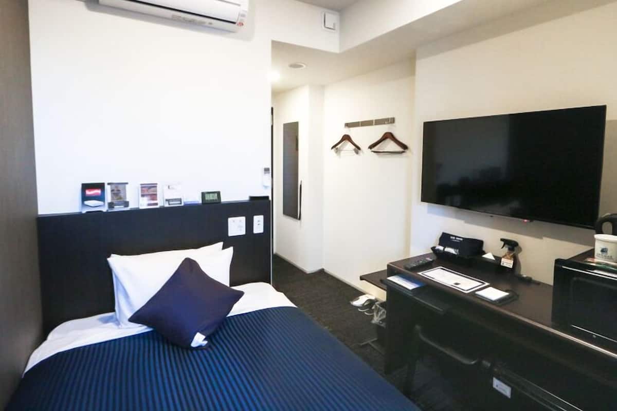 A hotel room with a bed, a desk, a flat-screen TV, and an air conditioning unit.