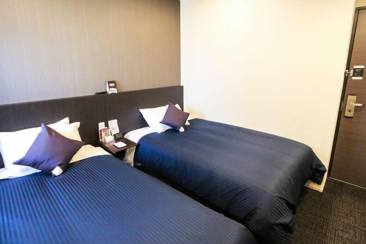 A hotel room with two beds, a nightstand, and a door.