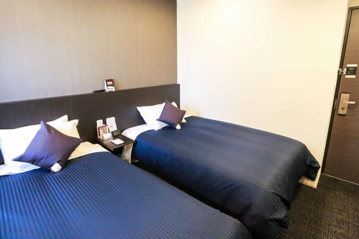 A hotel room with two beds, a nightstand, and a door.