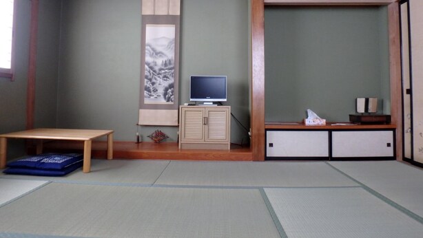 Una habitación japonesa tradicional con suelo de tatami, un escritorio de madera bajo, un televisor y un armario con espacio de almacenamiento.