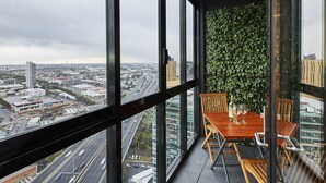 Un edificio alto con balcón que incluye una mesa y sillas, vistas de un paisaje urbano y una pared verde con follaje.