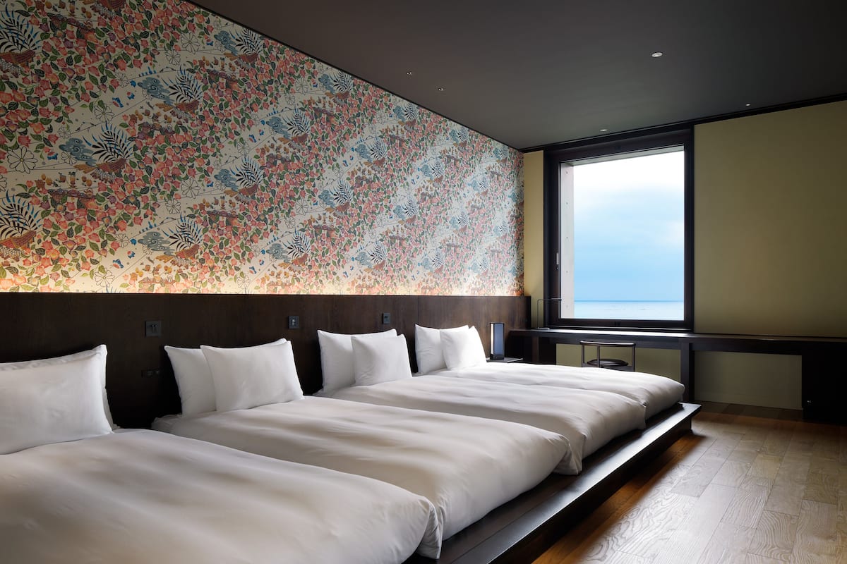 A hotel room with two beds, a large window, and a floral-patterned wall.