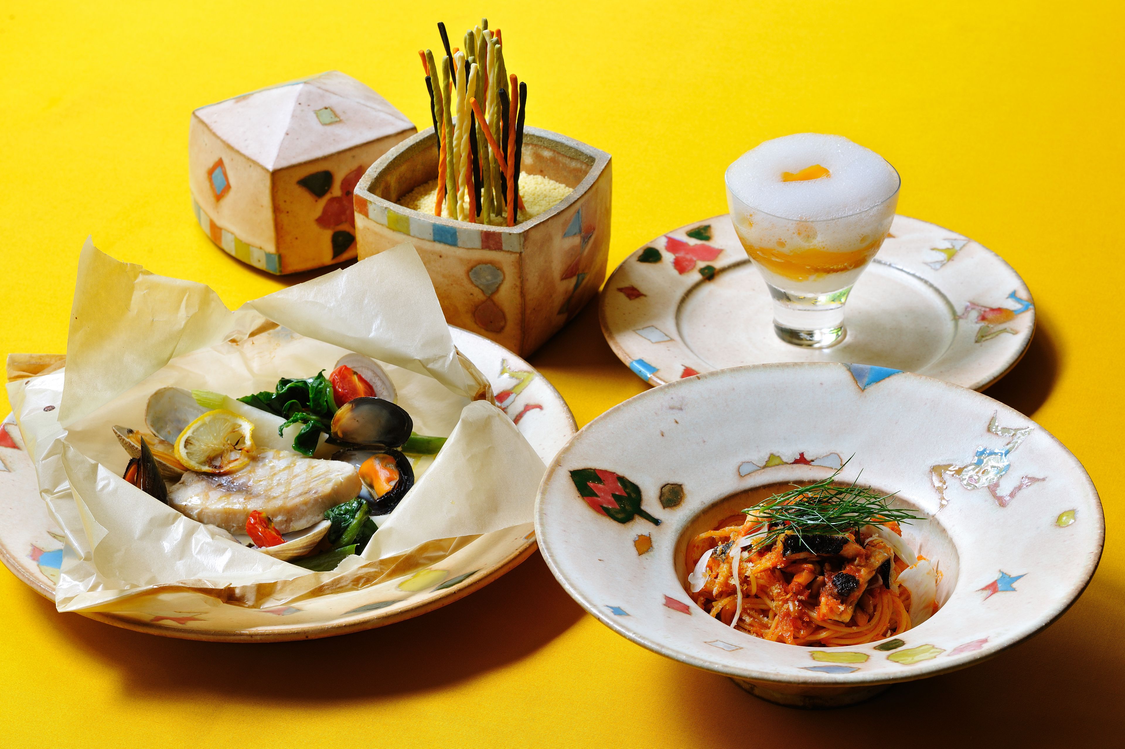 A table with various dishes, including seafood and pasta, and a glass of a light-colored beverage.