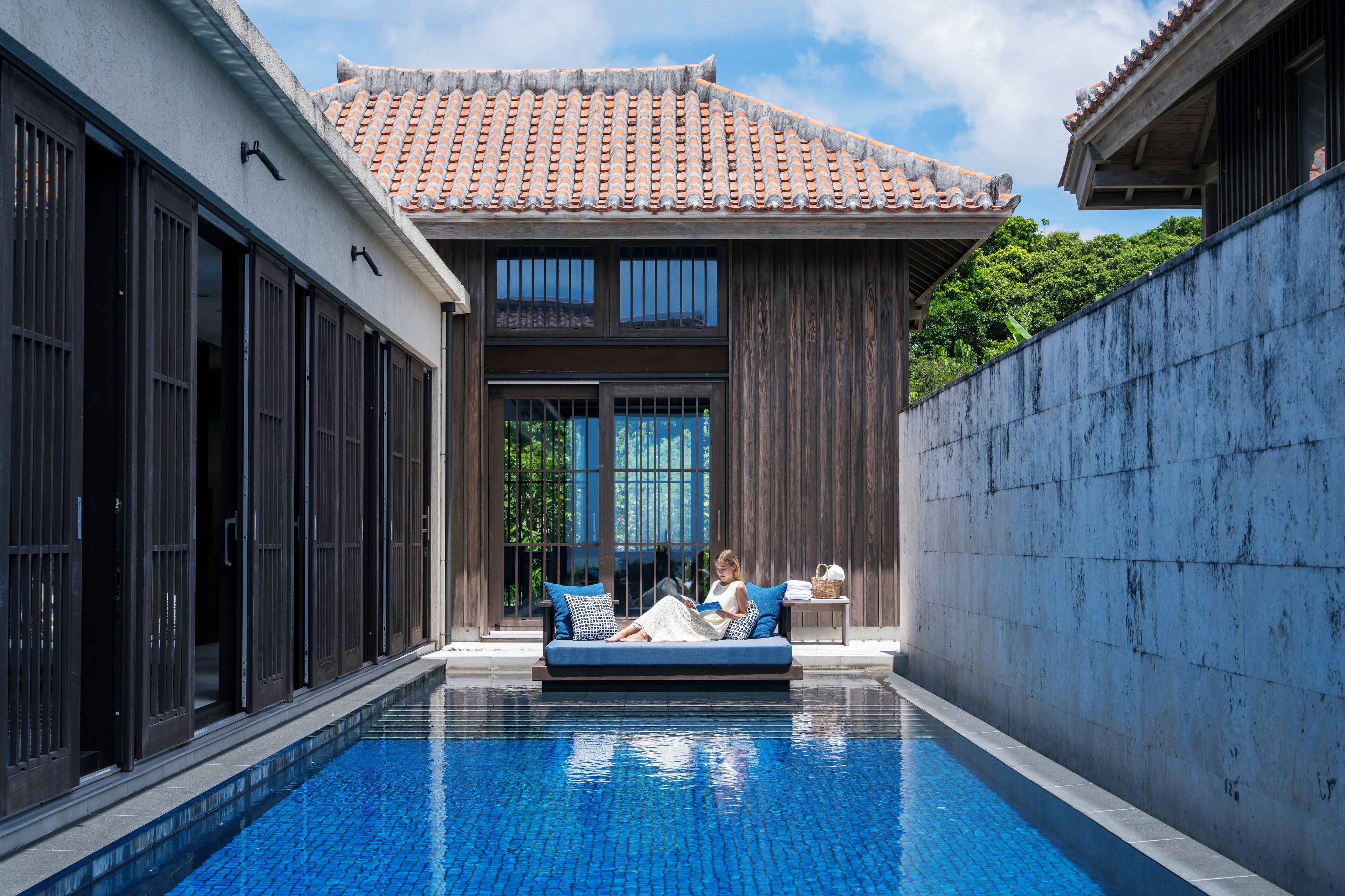 A poolside area with a blue-tiled pool, a wooden deck, and a traditional tiled roof structure.