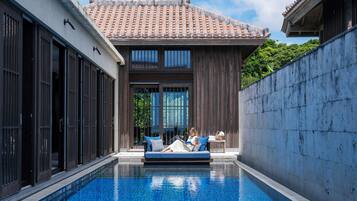 A poolside area with a blue-tiled pool, a wooden deck, and a traditional tiled roof structure.