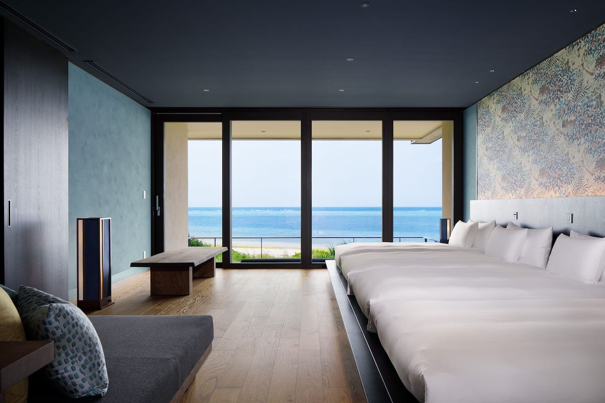 A modern bedroom with a large bed, a sofa, and a view of the ocean.