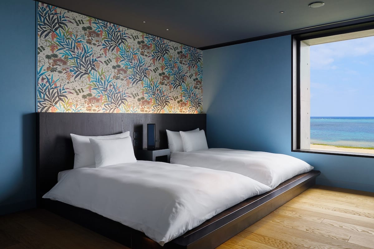 A modern hotel room with a large bed, a view of the ocean, and a colorful wall mural.