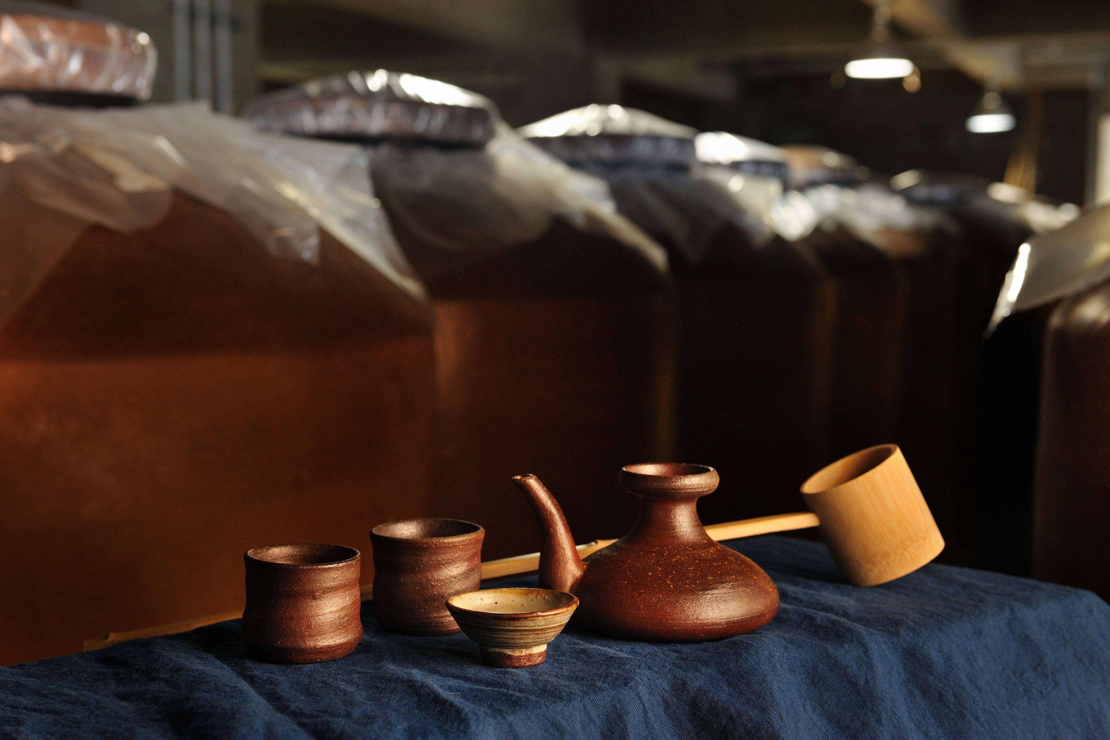Une table sur laquelle sont disposés divers objets en céramique et en bois, notamment des tasses et un pichet, le tout posé sur un tissu bleu.