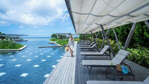A poolside area with lounge chairs, a wooden deck, and a view of the ocean. - HOSHINOYA Okinawa (Yomitan)