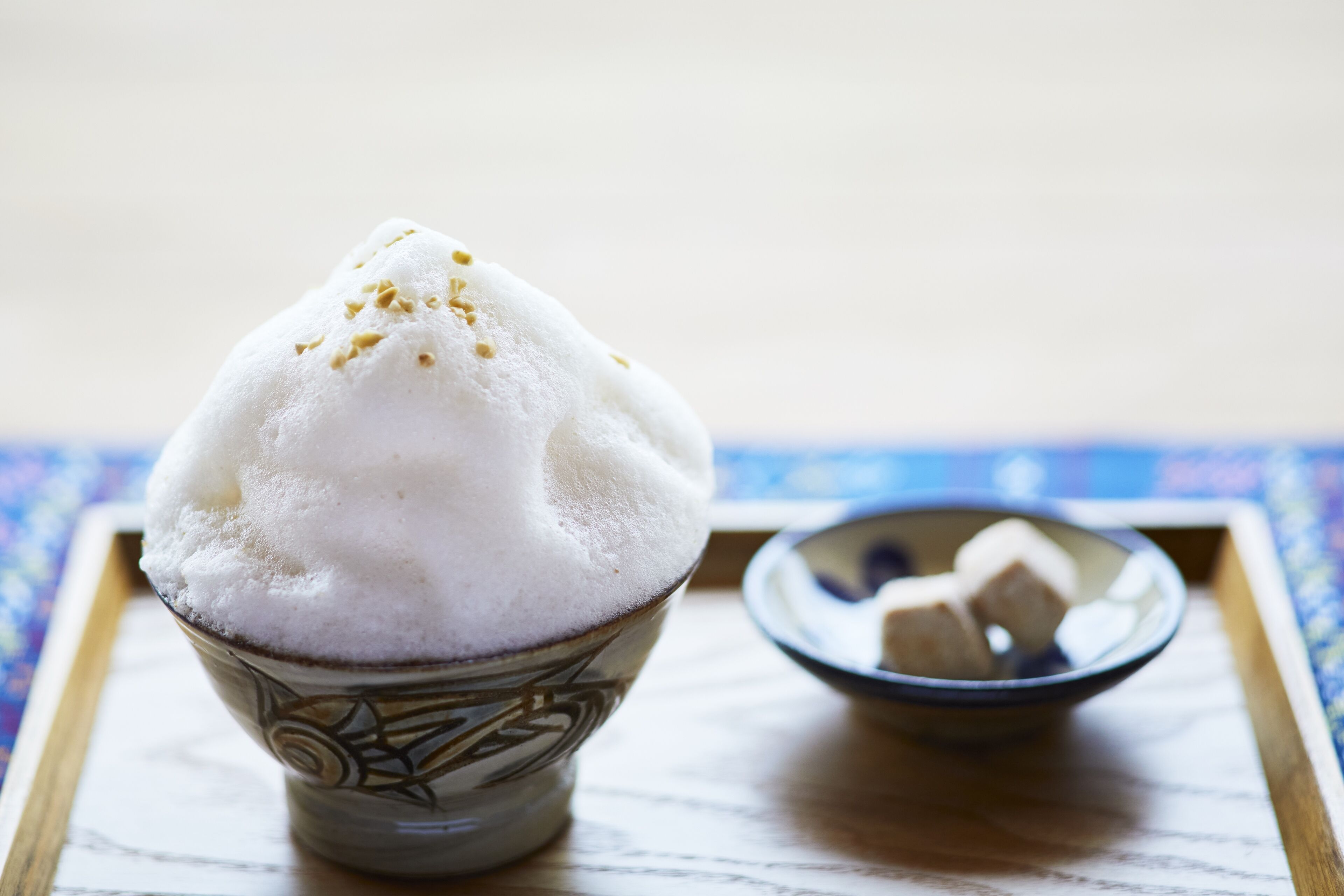 Un bol de glace pilée décorée d’un motif, posé sur un plateau sur lequel est disposée une nappe bleue à motifs.
