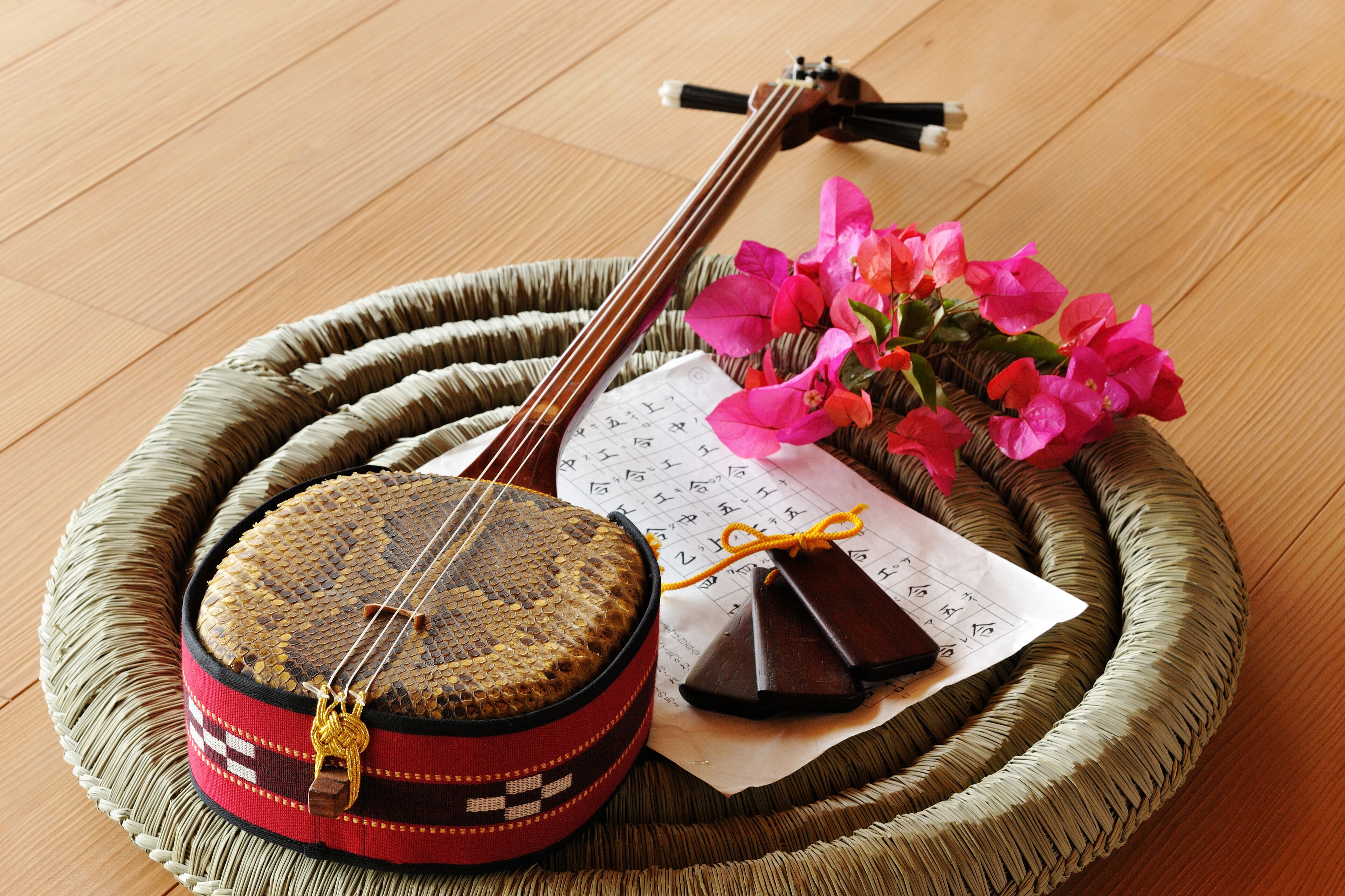 A traditional stringed instrument, a woven basket, and a piece of paper with text, all placed on a woven mat.