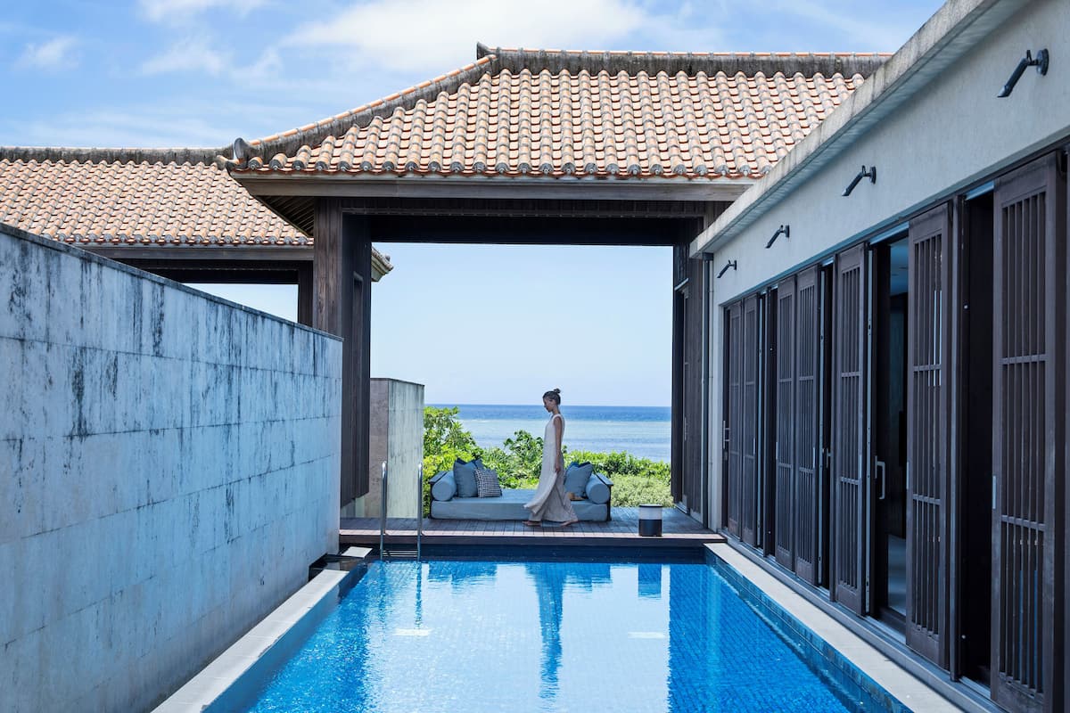 A pool area with a view of the ocean, a covered seating area, and a building with large windows.