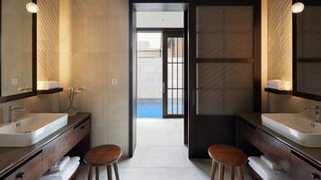 A modern bathroom with two sinks, wooden stools, and a large mirror.