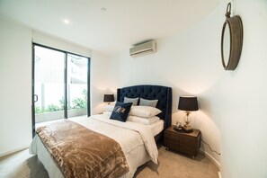 Ein Schlafzimmer mit einem großen Bett, einem Nachttisch, einer Wand-Klimaanlage und einer Glastür zum Balkon.