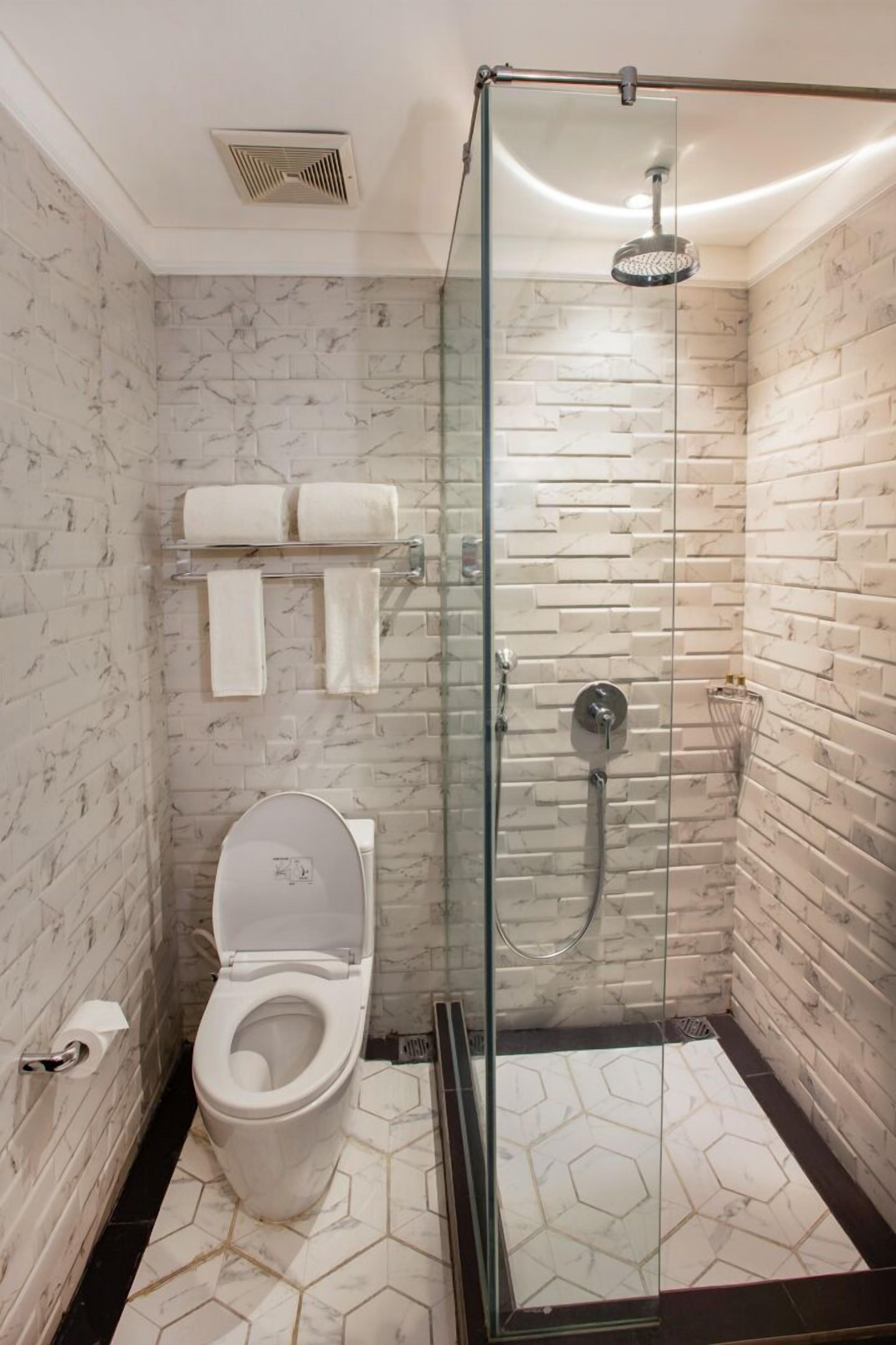 Un baño moderno con ducha envuelta en vidrio, inodoro y toallero con dos toallas.