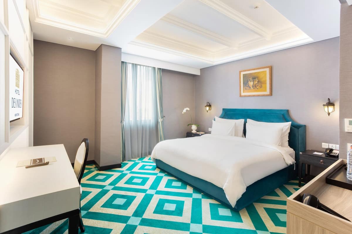 A hotel room with a bed, bedside tables, a desk, and a chair.