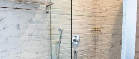 A modern bathroom with a glass-enclosed shower, white marble tiles, and a hexagonal floor pattern.