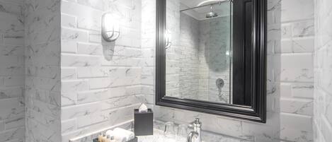 Un baño moderno con un lavamanos de mármol blanco, un espejo grande y un mueble de tocador negro.