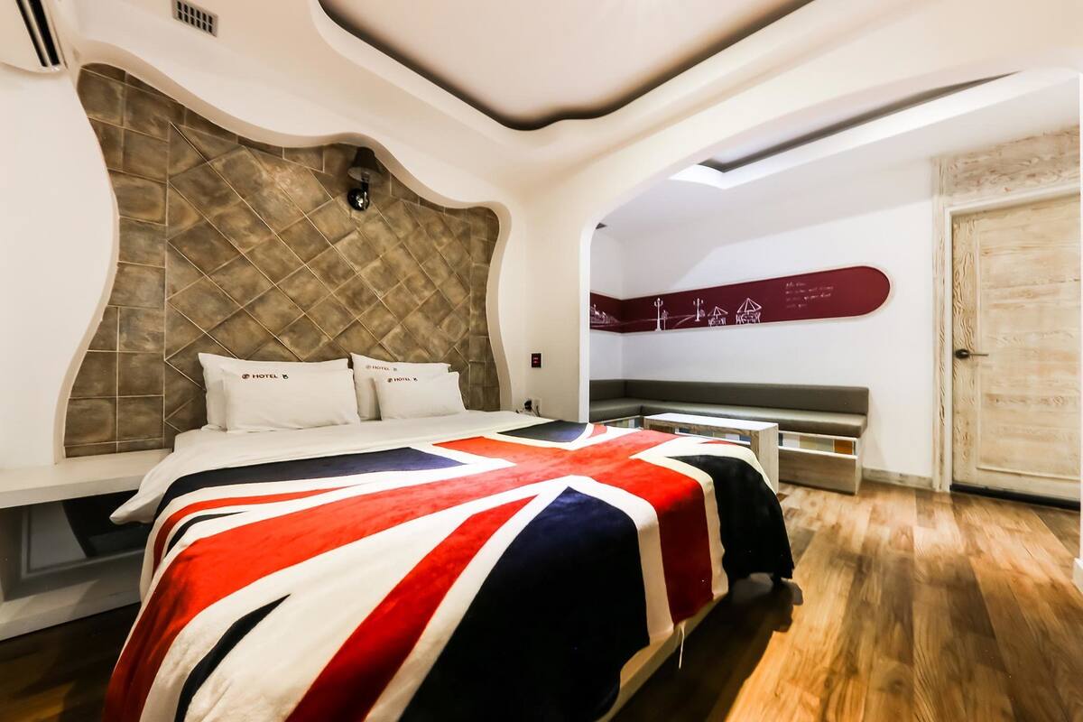 A hotel room with a large bed, a headboard with a diamond pattern, a wall-mounted sign, and a wooden door.