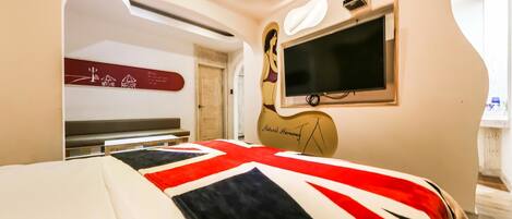 A bedroom with a bed, a television, a wall art piece, and a door leading to another room.