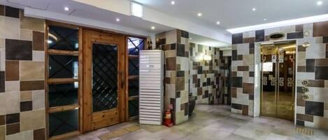 Un hall de hotel con suelo de baldosas, un extintor y una puerta de madera con paneles de vidrio.