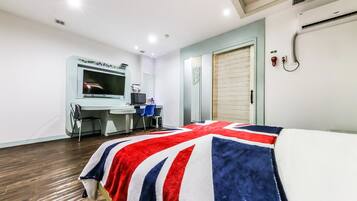 A hotel room with a bed, a desk, a chair, a television, and an air conditioning unit.