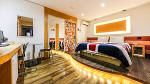 A modern hotel room with a wooden floor, a bed with a red, white, and blue striped blanket, a small bedside table, and a wall-mounted TV. - Born Hotel Cheongju (Cheongju)