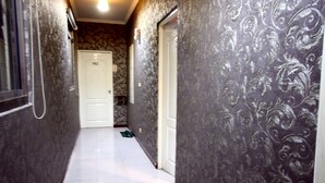 A narrow hallway with patterned wallpaper, a white door labeled "302", and green slippers on the floor. - Wen Mei Motel (Nantou)