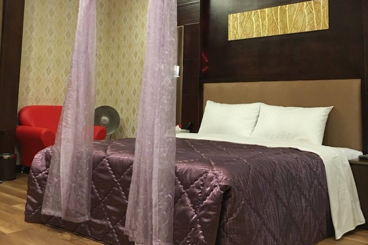 A bedroom with a four-poster bed, a red chair, and a wall-mounted fan.