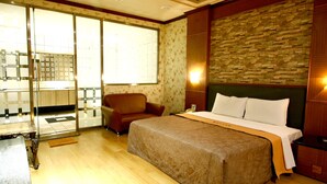 A hotel room with a large bed, a chair, a desk, and a view of the bathroom through a glass door. - Wen Mei Motel (Nantou)