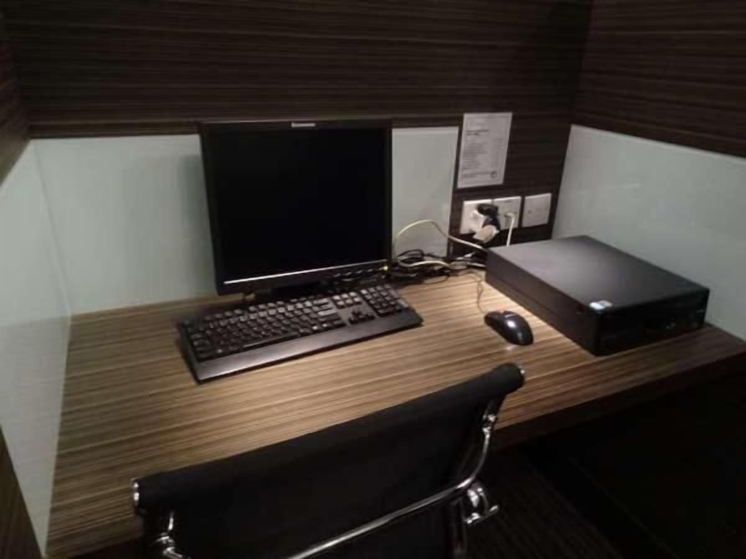 A wooden desk with a computer monitor, keyboard, mouse, and a black chair.