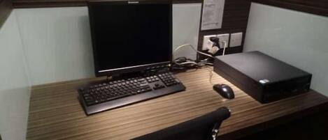 A wooden desk with a computer monitor, keyboard, mouse, and a black chair.