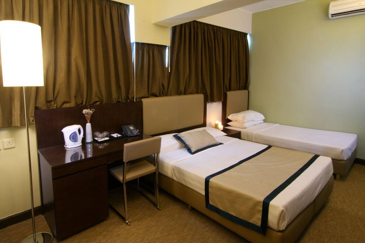 A hotel room with two beds, a desk, a chair, a lamp, and a bedside table with a phone and a vase.