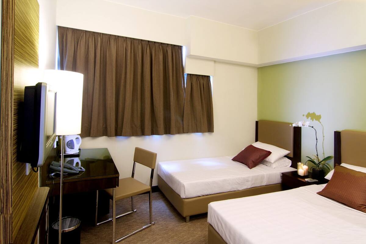 A hotel room with two beds, a desk with a lamp, a chair, a TV, and a potted orchid.