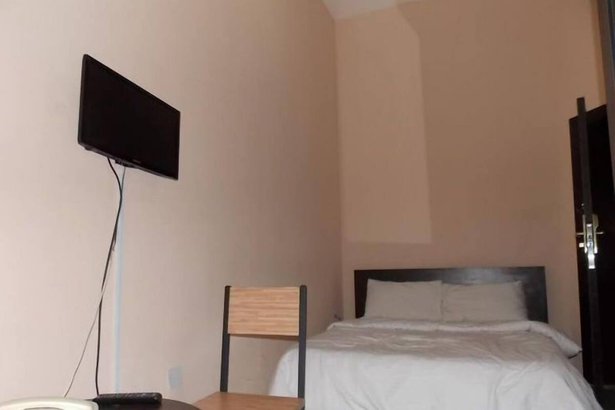 Une chambre à coucher avec un lit, une chaise, un téléviseur fixé au mur et une porte.