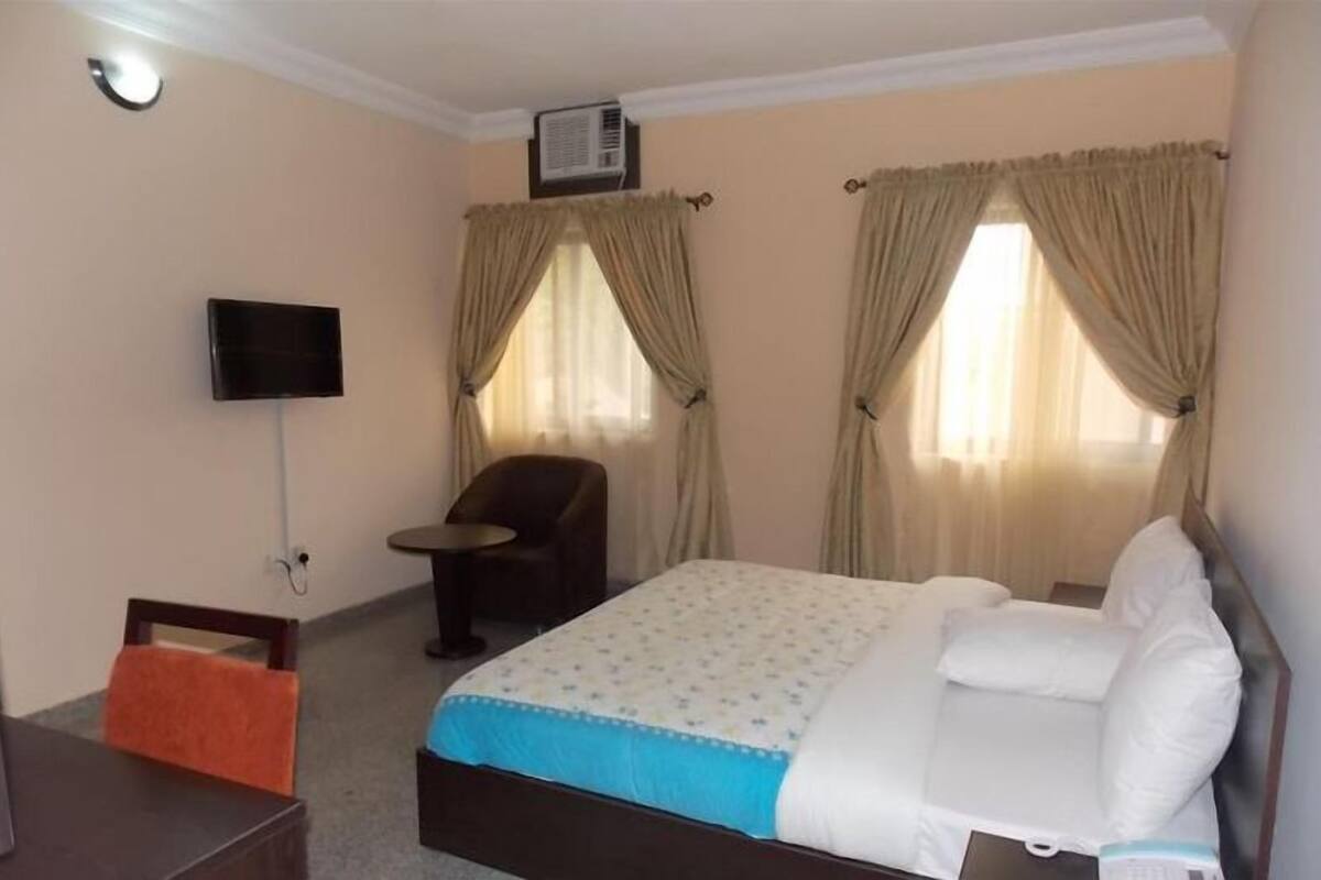 Une chambre d’hôtel avec un lit, une chaise, une télévision et des rideaux.