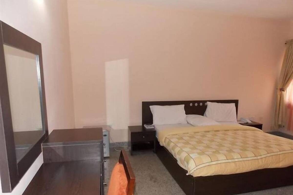 Une chambre d’hôtel avec un lit, une table de chevet, une commode et un miroir.
