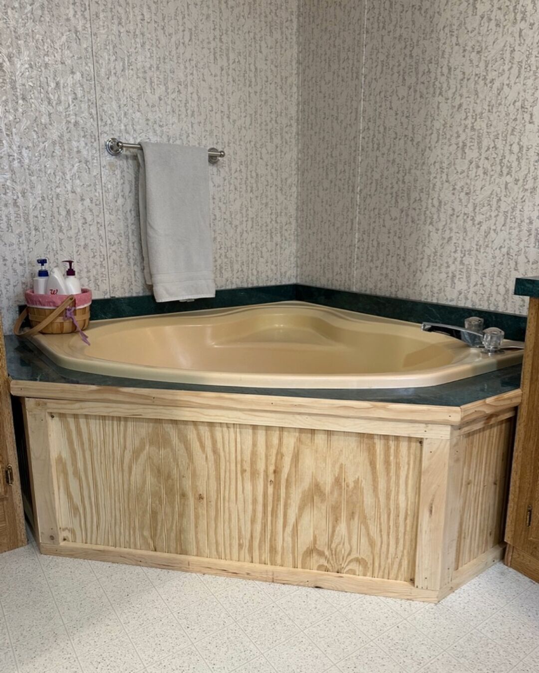 Una bañera de madera con detalle verde, una toalla colgada en un aro metálico y una cesta con artículos de tocador.