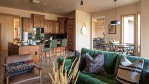 A spacious living area with a green sofa, a wooden dining table, and a kitchen with wooden cabinets.