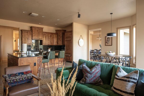 A spacious living area with a green sofa, a wooden dining table, and a kitchen with wooden cabinets. - Powell by AvantStay | Secluded Home only 10 Mins from DT Bend w/ Hot Tub (Bend)
