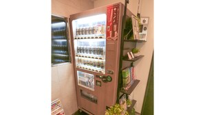 A vending machine with various beverages and snacks, a small plant, and a few books on a shelf. - Hotel Live Max Tokyo Kanda Station (Tokyo)