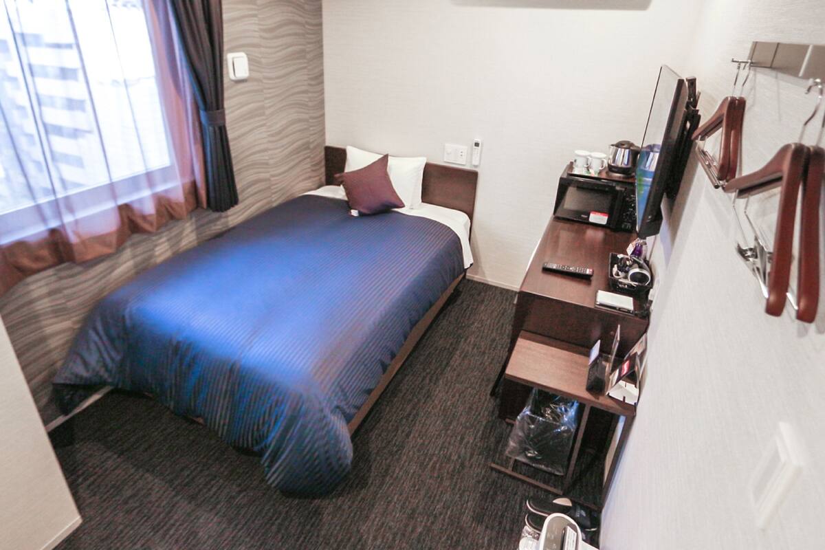 Una habitación de hotel con una cama, un escritorio con computadora, un televisor y un espejo.