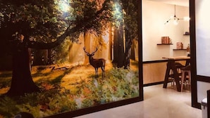 A room with a large wall mural of a forest scene, a dining area with a table and chairs, and a hanging light fixture. - Cheng Lan Hotel (Yuchi)