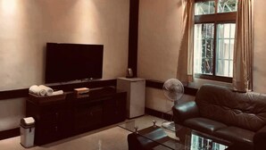 A modern living room with a flat-screen TV, a leather sofa, a glass coffee table, a small cabinet, and a standing fan. - Cheng Lan Hotel (Yuchi)